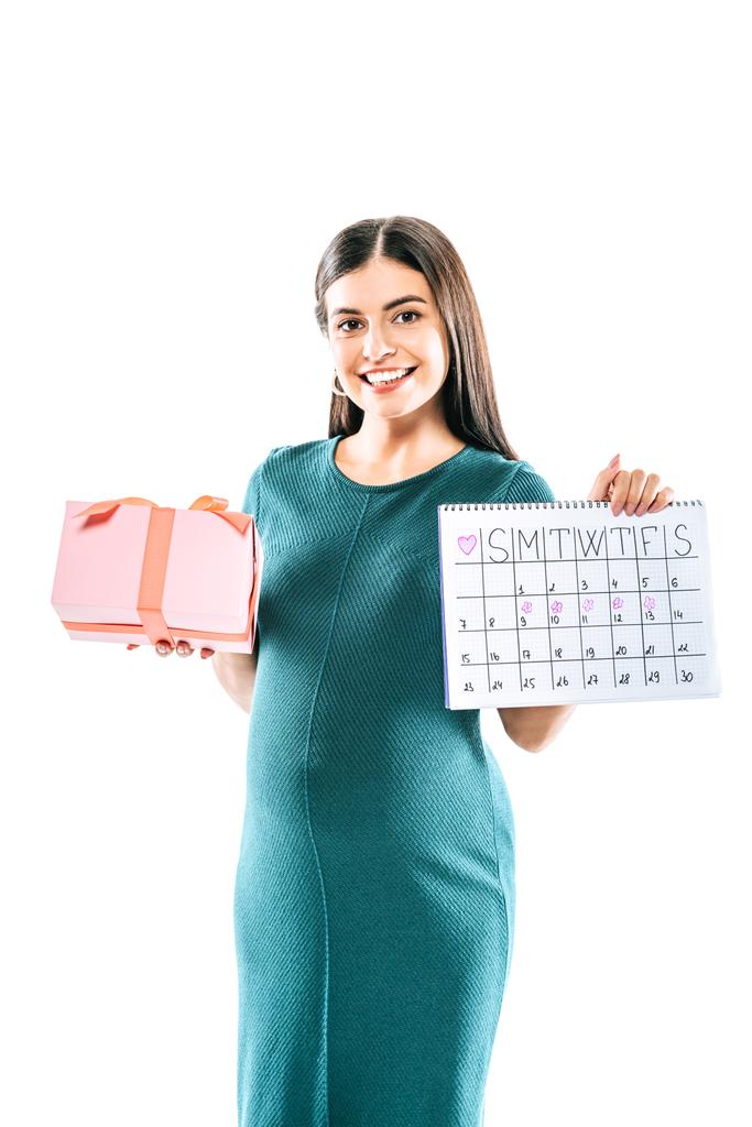 усміхнена вагітна дівчина тримає подарунок і календар періоду ізольовано на білому
 - Фото, зображення