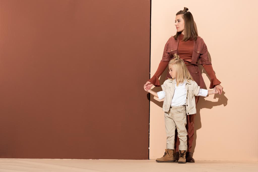 мила дочка і приваблива мати тримає руки на бежевому і коричневому фоні
  - Фото, зображення