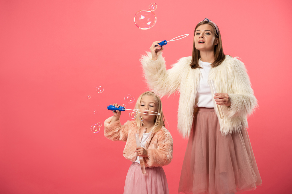 daughter and smiling mother blowing soap bubbles on pink background  - 写真・画像