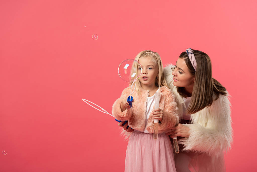 dochter en lachende moeder blazen zeepbellen geïsoleerd op roze - Foto, afbeelding