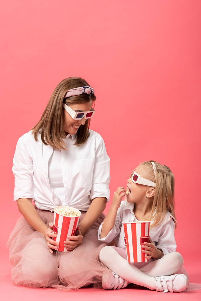 dcera jíst popcorn a usmívající se matka v 3D brýle na růžovém pozadí  - Fotografie, Obrázek