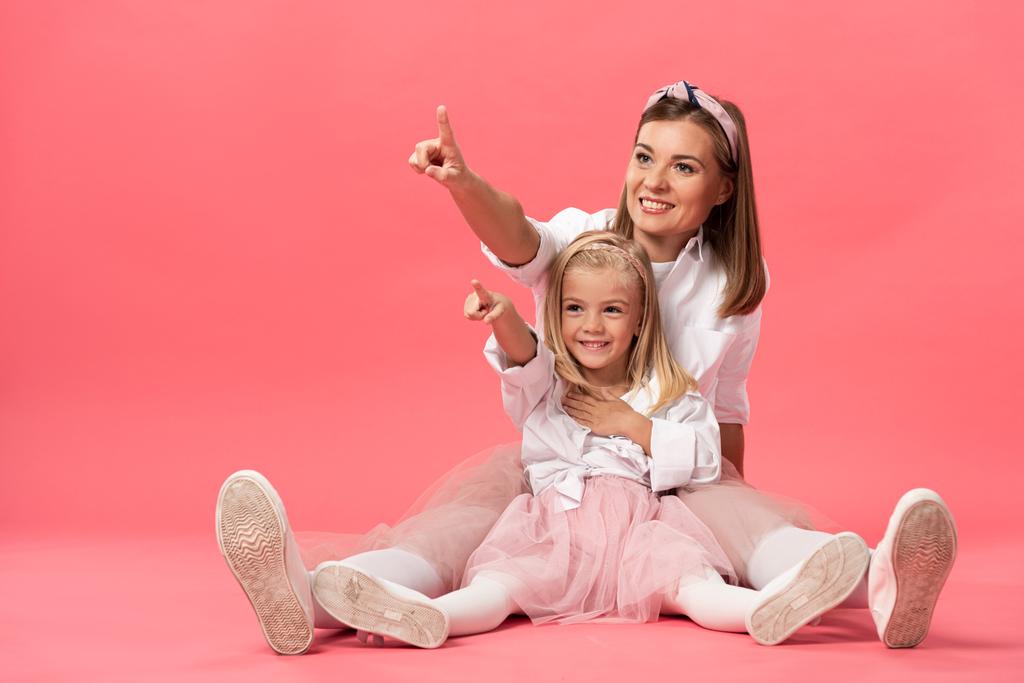 Lächelnde Tochter und Mutter zeigen mit den Fingern auf rosa Hintergrund  - Foto, Bild