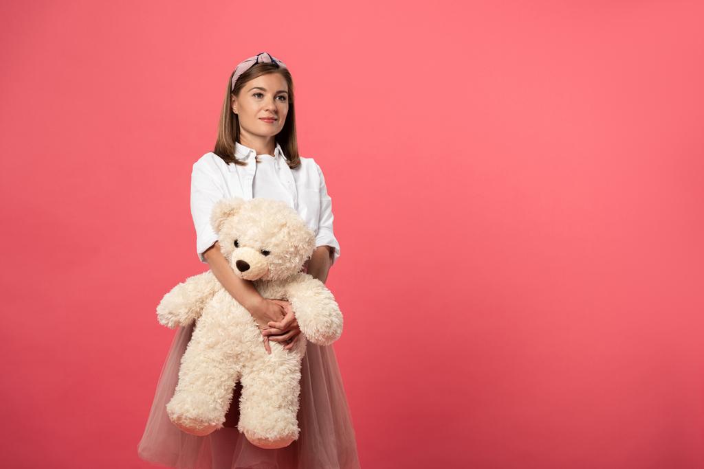 attractive and smiling woman holding teddy bear isolated on pink - Photo, Image