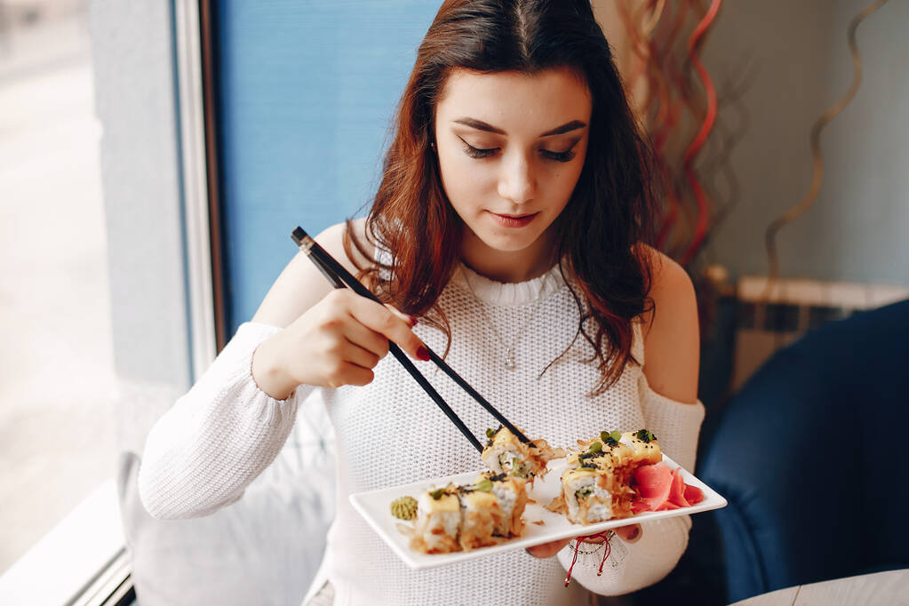 Γυναίκα κάθεται στο τραπέζι και τρώει σούσι στο καφέ - Φωτογραφία, εικόνα