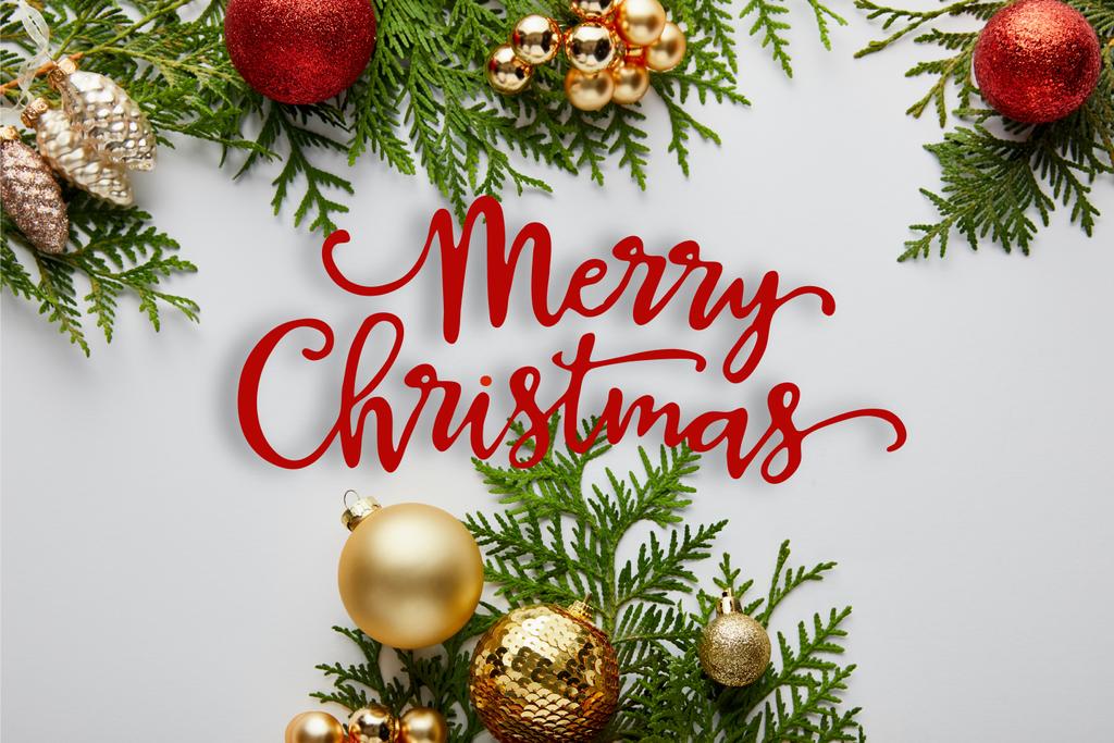 Rahmen aus goldglänzendem und rotem Weihnachtsschmuck auf grünen Thuja-Zweigen isoliert auf weiß mit froher Weihnachtsillustration - Foto, Bild