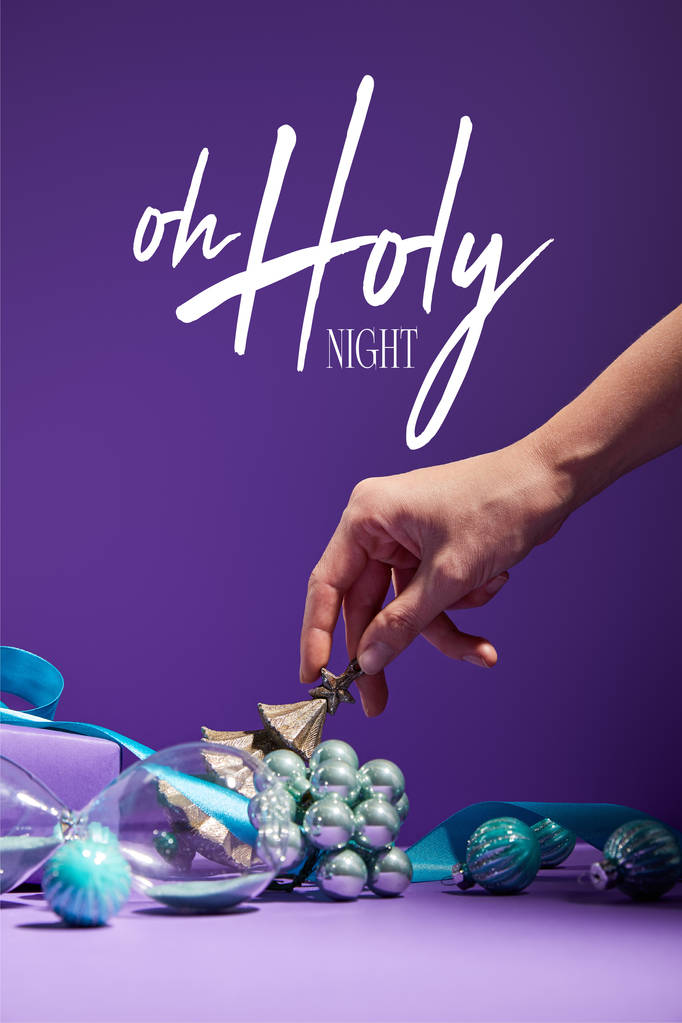 abgeschnittene Ansicht der Frau berühren Weihnachtsdekoration und Sanduhr auf lila Hintergrund mit o heilige Nacht Illustration verstreut - Foto, Bild