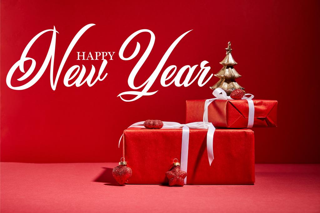 czerwone pudełka i dekoracyjne złote choinki z bombkami na czerwonym tle z szczęśliwego nowego roku liternictwo - Zdjęcie, obraz