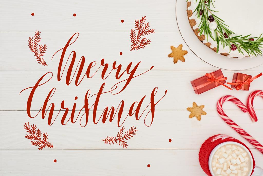 vista superior de pastel de Navidad con glaseado en mesa de madera blanca con bastones de caramelo, regalos y cacao con ilustración de Feliz Navidad
 - Foto, imagen