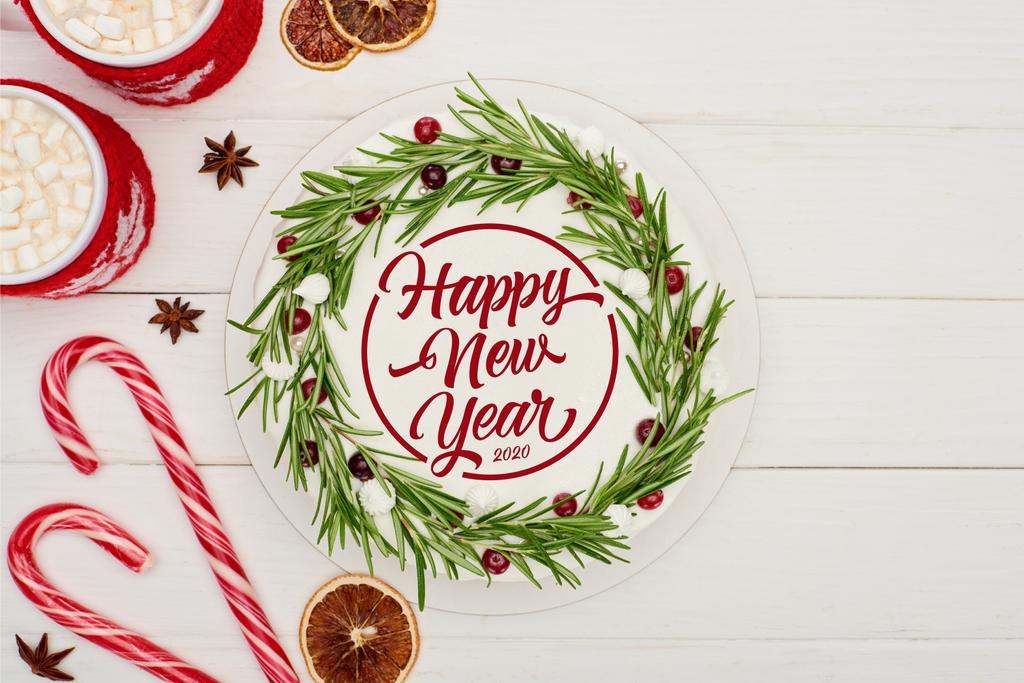 top view of candy canes, two cups of cocoa and christmas pie with icing on white wooden table with happy new year lettering - Photo, Image