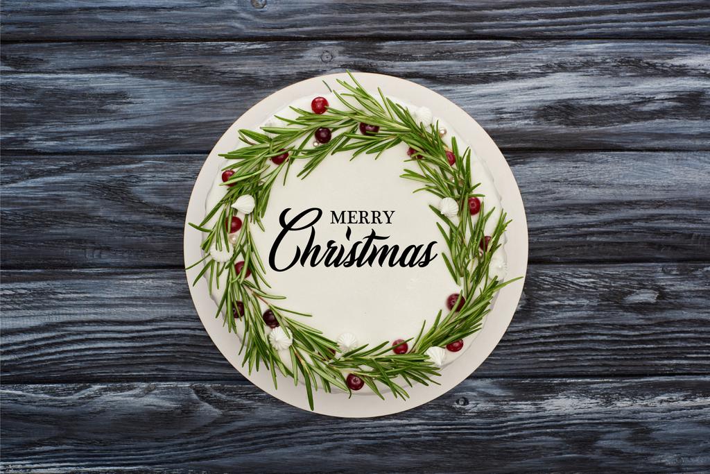 top view of traditional christmas pie with white icing, rosemary and cranberries on dark wooden table with Merry Christmas illustration - 写真・画像