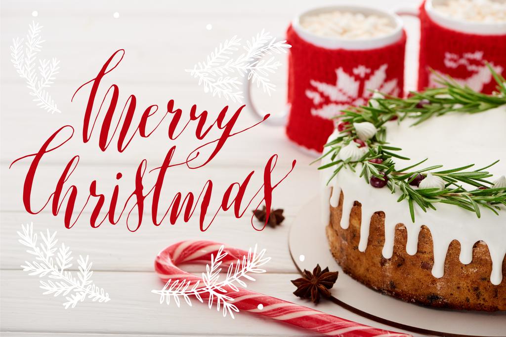 bastón de caramelo, pastel de Navidad con glaseado y dos tazas de cacao con malvaviscos en una mesa de madera blanca con ilustración de Feliz Navidad
 - Foto, Imagen