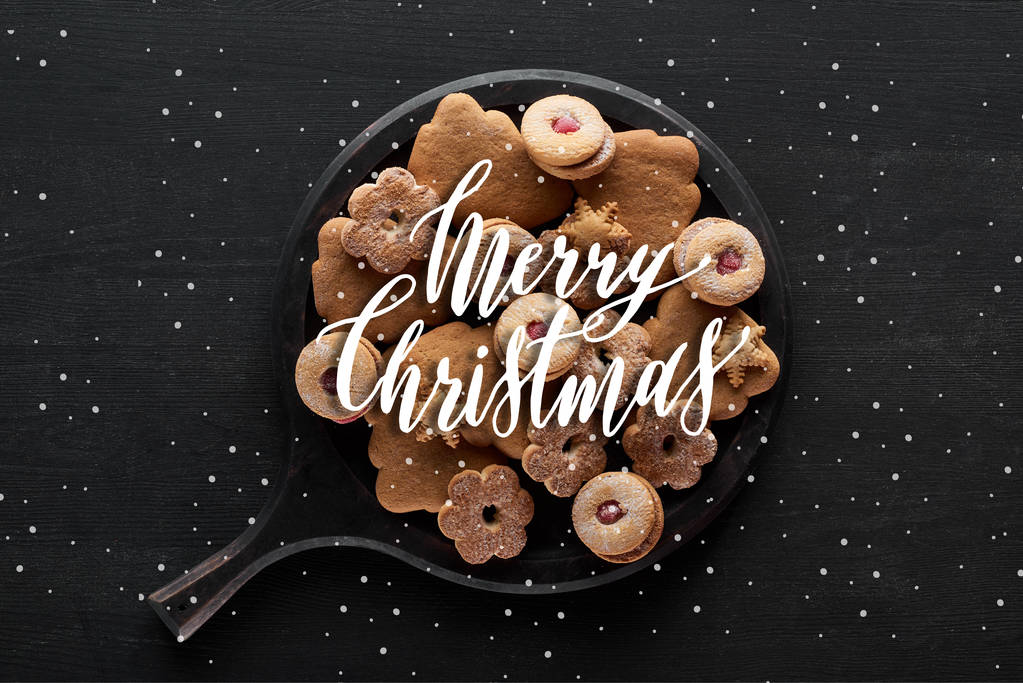 vista superior de galletas de Navidad en bandeja sobre mesa de madera negra con ilustración de Feliz Navidad y nevadas
 - Foto, imagen