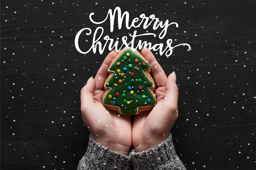 cropped view of woman holding baked Christmas tree cookie in hands with Merry Christmas illustration - Фото, зображення