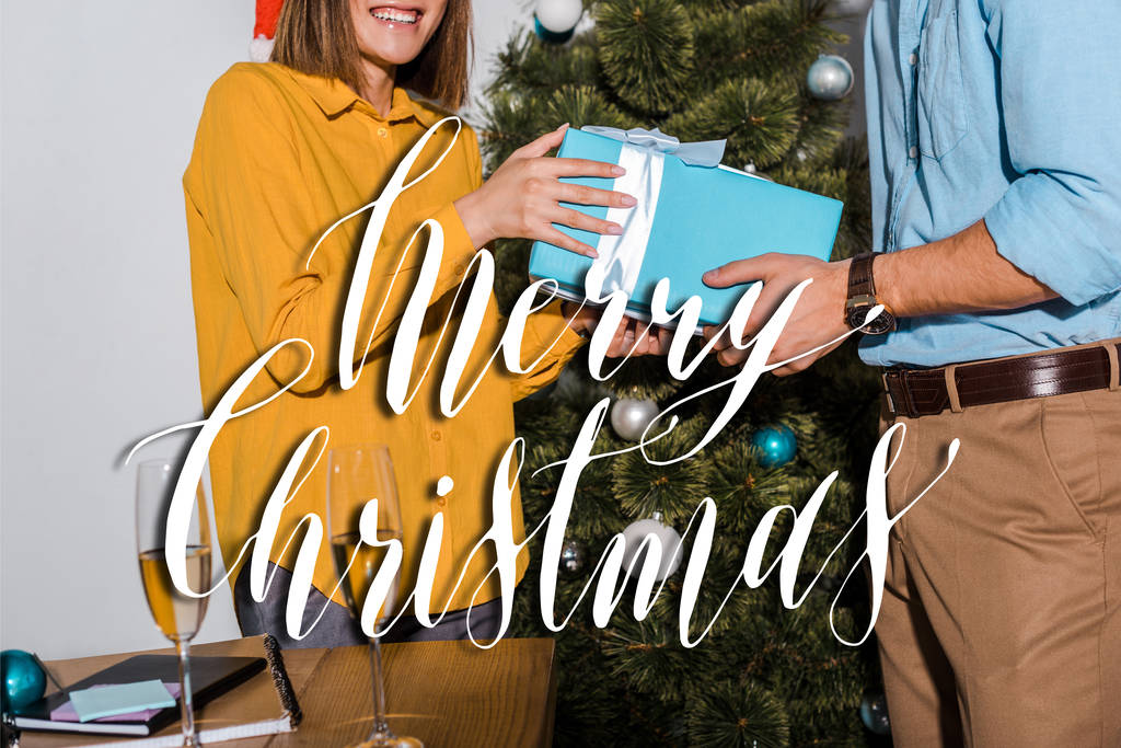 περικοπή άποψη του άνδρα δίνοντας δώρο στη γυναίκα κοντά στο χριστουγεννιάτικο δέντρο με χαρούμενα Χριστούγεννα εικονογράφηση  - Φωτογραφία, εικόνα