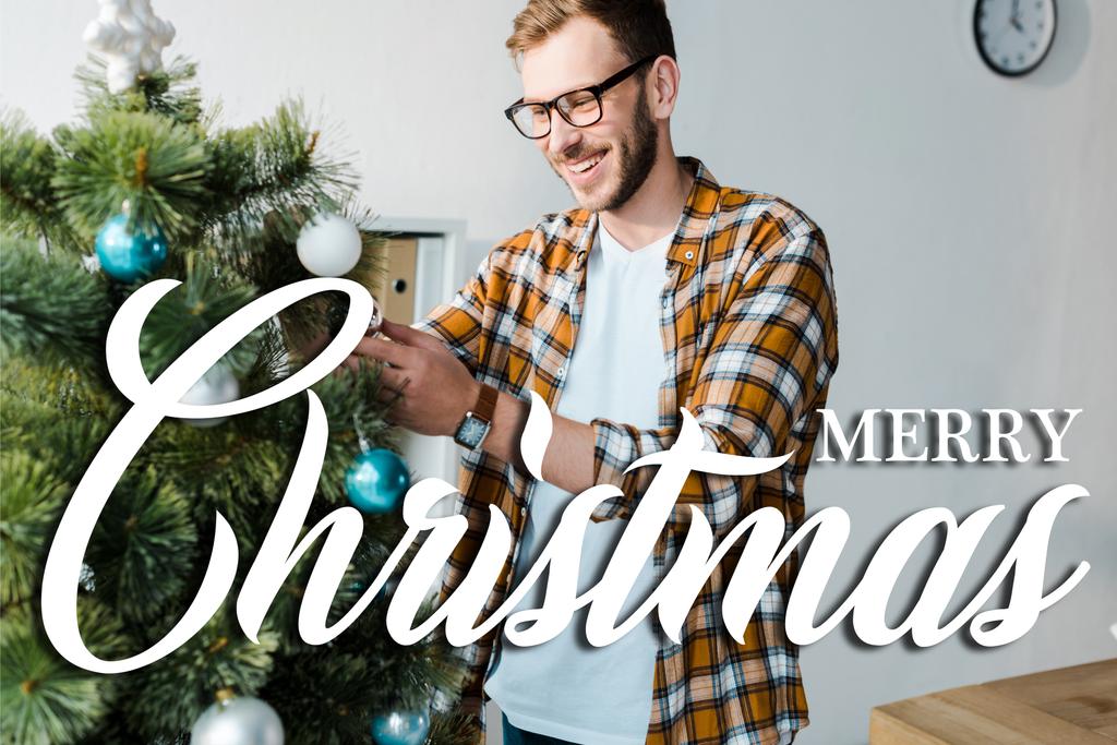 happy bearded man in glasses decorating christmas tree in office with merry christmas illustration  - Photo, Image