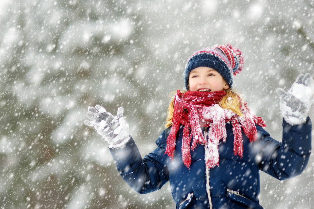 Adorable young girl having fun in beautiful winter park during snowfall. Cute child playing in a snow. Winter activities for family with kids. - Photo, Image