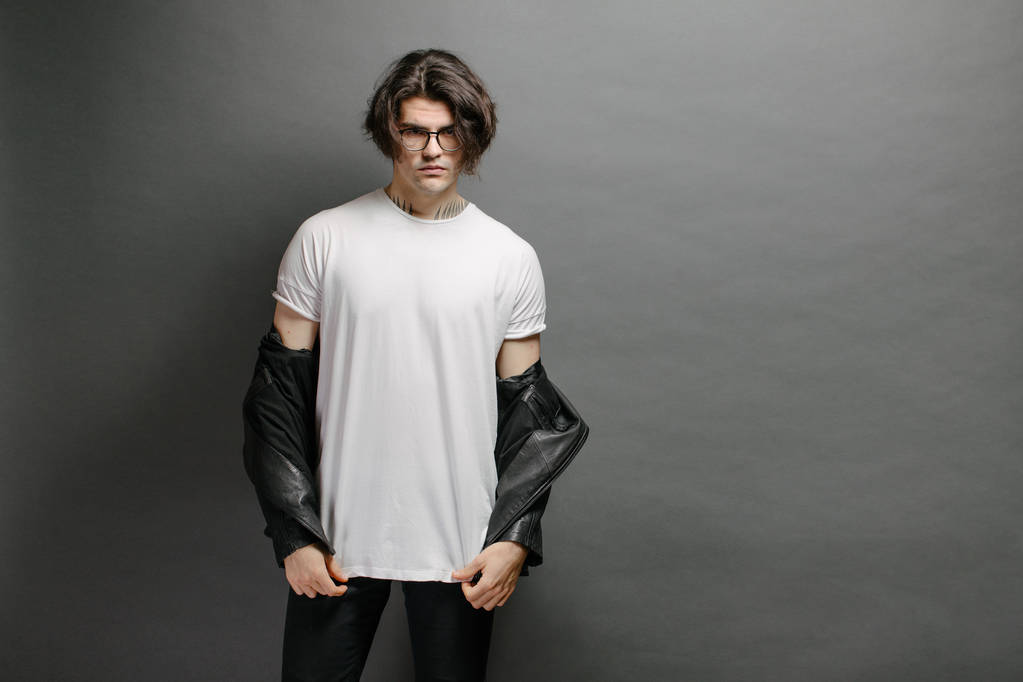 Hipster knap mannelijk model met bril in wit wit wit t-shirt en zwarte jeans met ruimte voor uw logo of ontwerp in casual urban stijl - Foto, afbeelding
