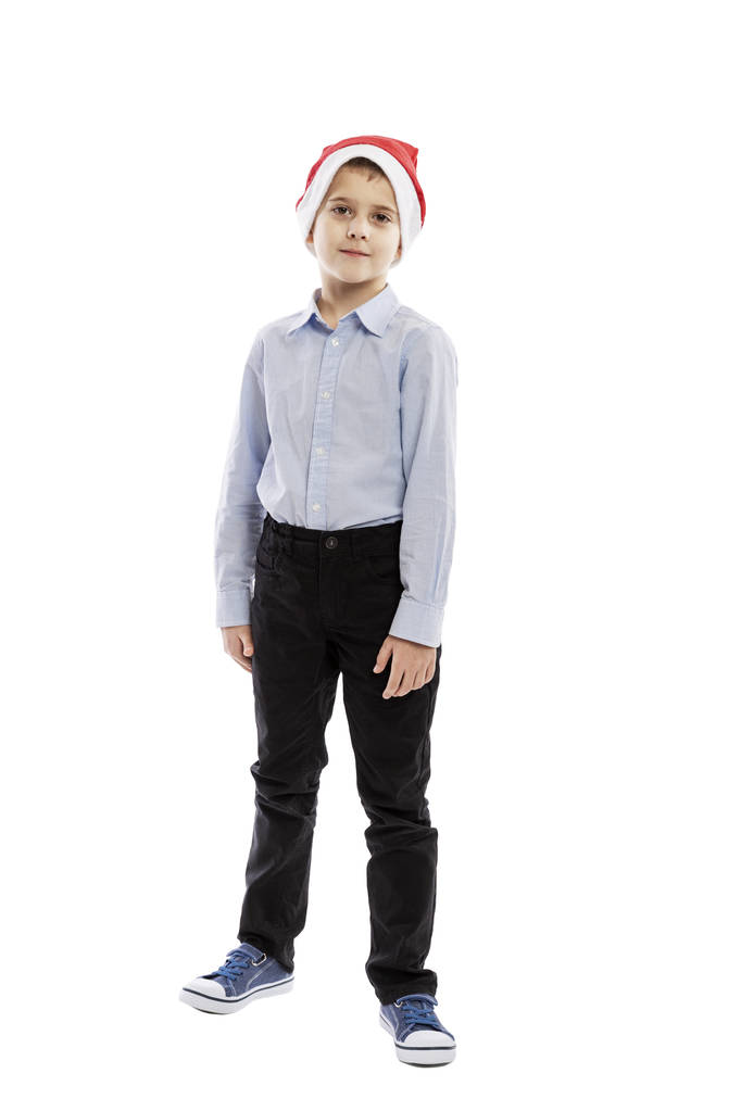 Милий школяр у капелюсі Санта Клауса стоїть. Висота. Ізольовані на білому тлі.  - Фото, зображення