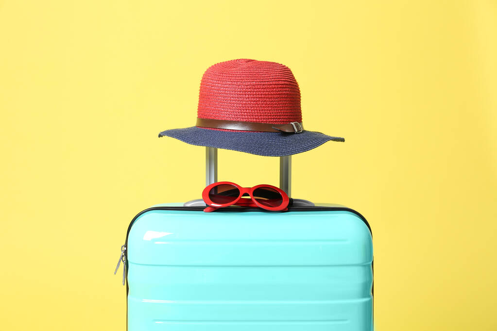 Turkoois koffer met zonnebril en hoed op gele achtergrond - Foto, afbeelding