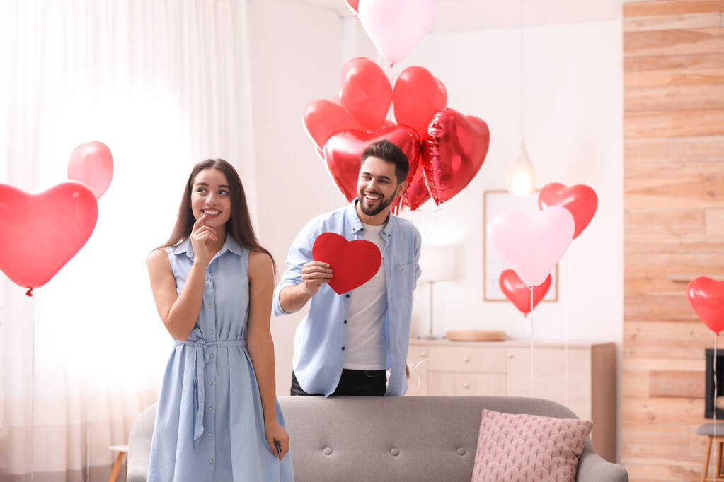 Υπέροχο ζευγάρι με μπαλόνια σε σχήμα καρδιάς στο σαλόνι. Γιορτή του Αγίου Βαλεντίνου - Φωτογραφία, εικόνα