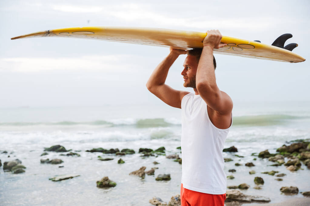 Mężczyzna surfer z surfingu na plaży na zewnątrz. - Zdjęcie, obraz