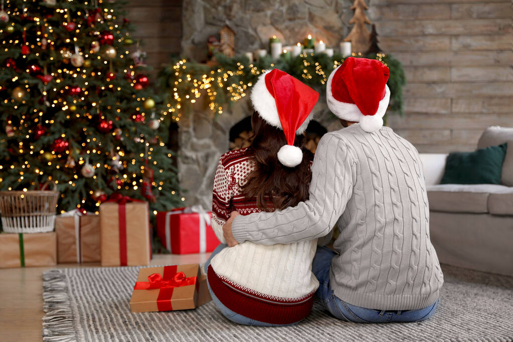 Ευτυχισμένο νεαρό ζευγάρι που φοράει καπέλα Σάντα στο σαλόνι διακοσμημένο για τα Χριστούγεννα - Φωτογραφία, εικόνα