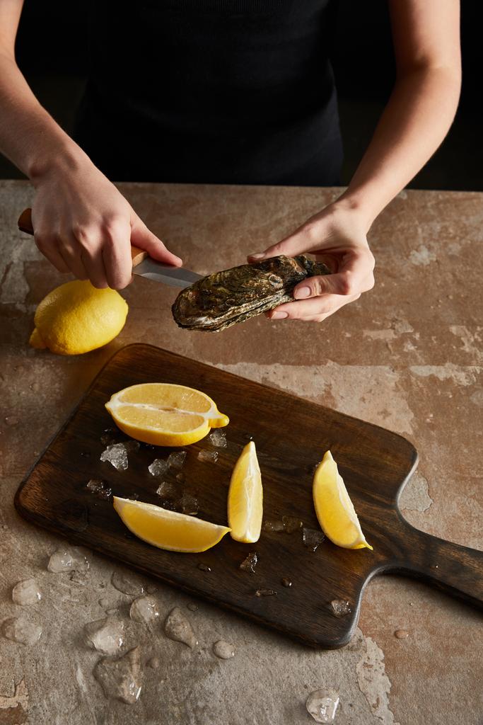 レモンの近くで牡蠣を開きながらナイフを持つ女の姿を切り取った  - 写真・画像