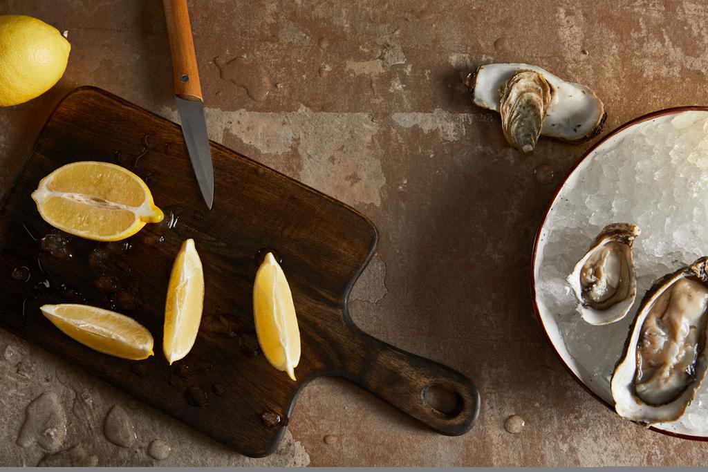 vista superior de limones frescos en la tabla de cortar cerca de ostras en tazón con cubitos de hielo
  - Foto, imagen