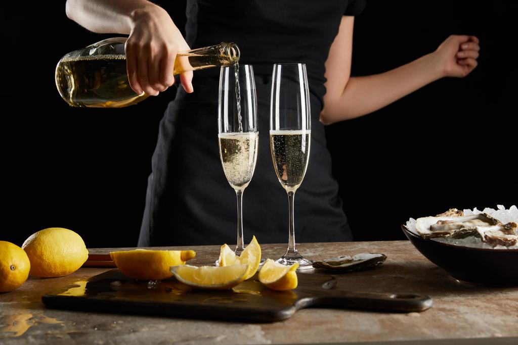 przycięty widok kobiety lejącej wino musujące w kieliszku szampana w pobliżu ostryg w misce z lodem izolowanym na czarno  - Zdjęcie, obraz