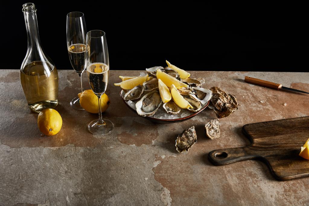champagne glasses with sparkling wine near bottle, oysters and lemons in bowl isolated on black  - Photo, Image