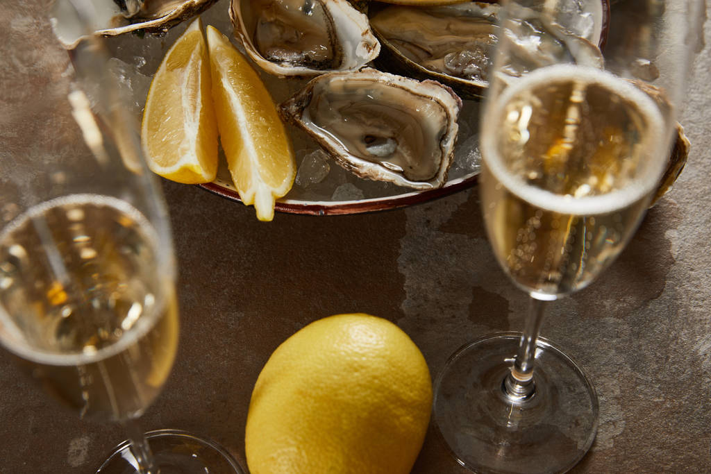foyer sélectif d'huîtres et de citrons dans un bol avec de la glace près de verres à champagne avec du vin mousseux
  - Photo, image