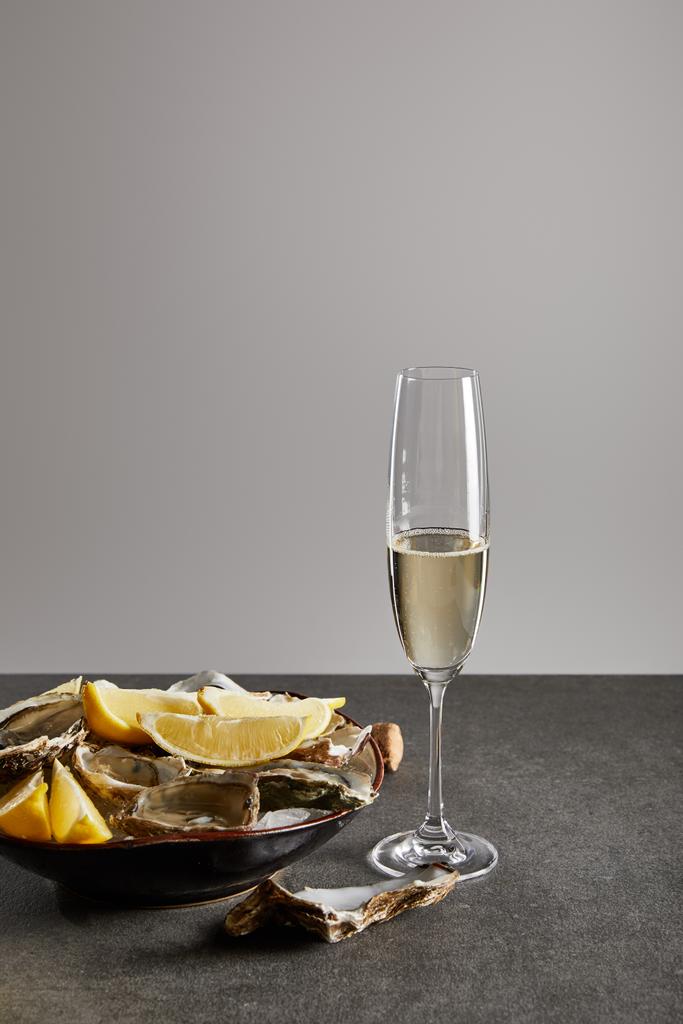 delicious oysters and lemons in bowl with ice near champagne glass with sparkling wine isolated on grey  - Photo, Image
