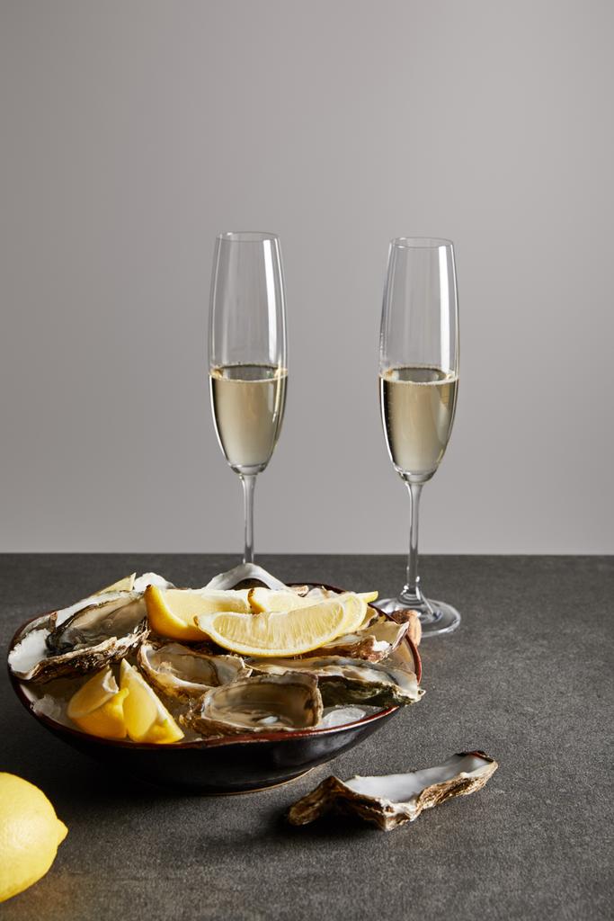 champagneglazen met mousserende wijn bij heerlijke oesters en citroenen in kom geïsoleerd op grijs  - Foto, afbeelding