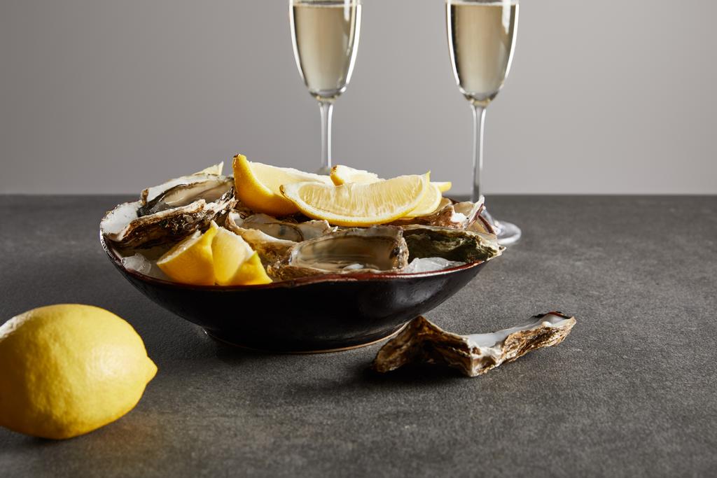 selective focus of delicious oysters and lemons in bowl near champagne glasses with sparkling wine isolated on grey  - Photo, Image