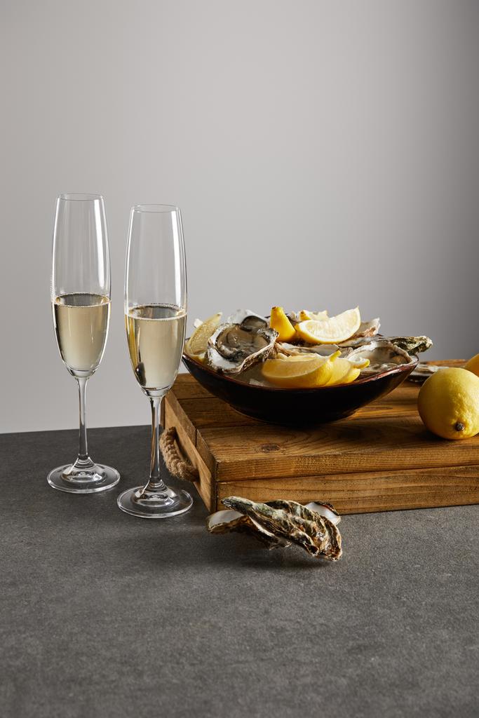 ostrygi i świeże cytryny w misce w pobliżu kieliszków do szampana z winem musującym izolowanym na szaro  - Zdjęcie, obraz