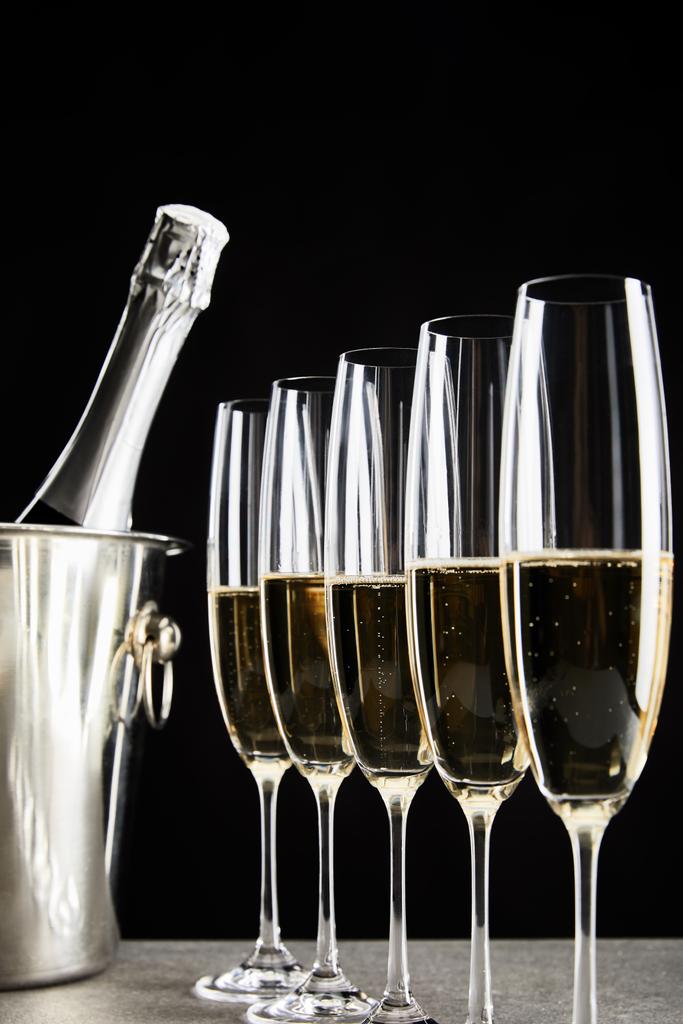 selective focus of champagne glasses with sparkling wine near bottle in ice bucket isolated on black  - Photo, Image