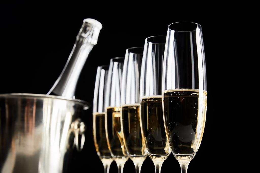 селективный фокус бокалов шампанского с игристым вином возле ведра со льдом с бутылкой, изолированной на черном
 - Фото, изображение