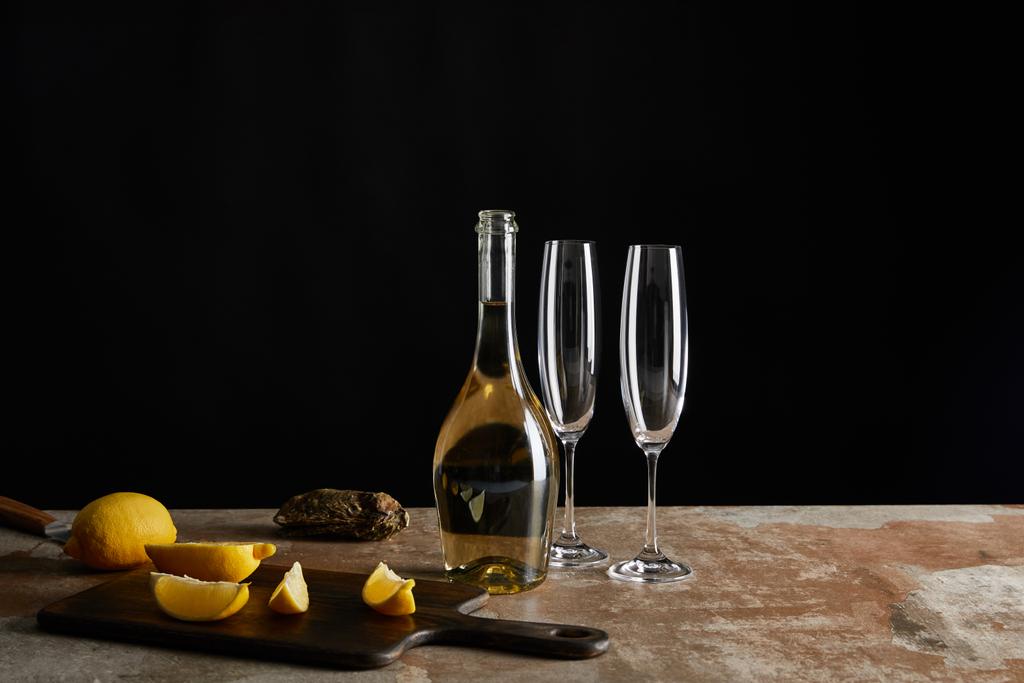 νόστιμο στρείδι με κέλυφος κοντά σε λεμόνια και μπουκάλι με αφρώδες κρασί που απομονώνονται σε μαύρο  - Φωτογραφία, εικόνα