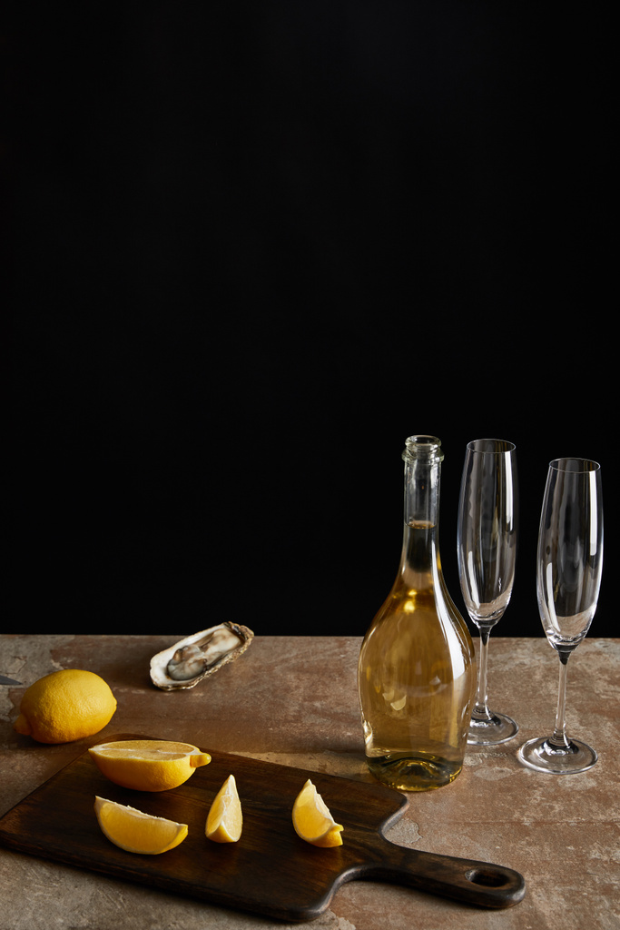 νόστιμο στρείδι κοντά σε λεμόνια και μπουκάλι με αφρώδες κρασί που απομονώνονται σε μαύρο  - Φωτογραφία, εικόνα