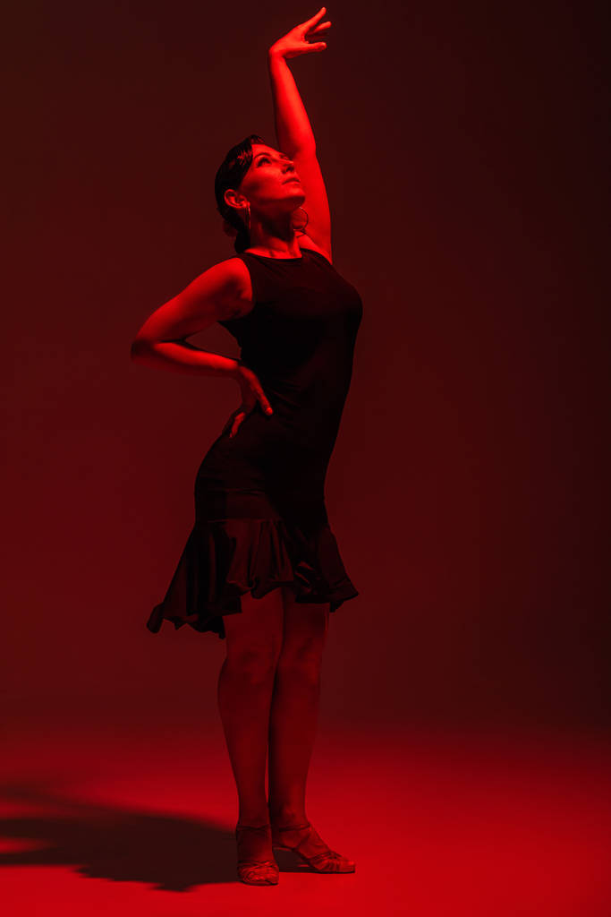 kecses táncos fekete ruhában tangót ad elő sötét háttéren piros megvilágítással - Fotó, kép
