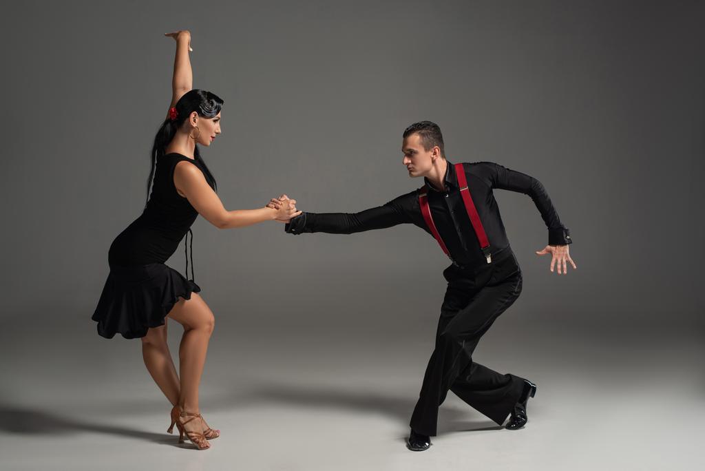 stylische Tänzer in schwarzer Kleidung, die sich beim Tanzen auf grauem Hintergrund anschauen - Foto, Bild