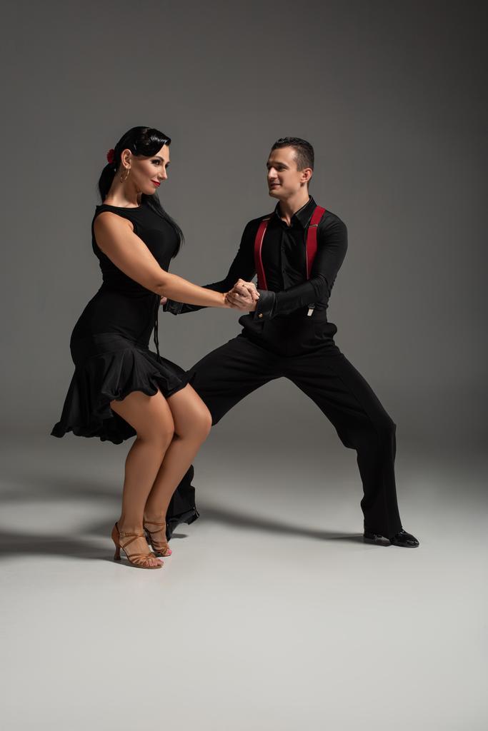 две улыбающиеся танцовщицы в черной одежде исполняют танго на сером фоне
 - Фото, изображение