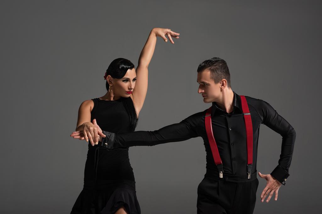 elegant couple of dancers looking at each other while performing tango isolated on grey - Photo, Image