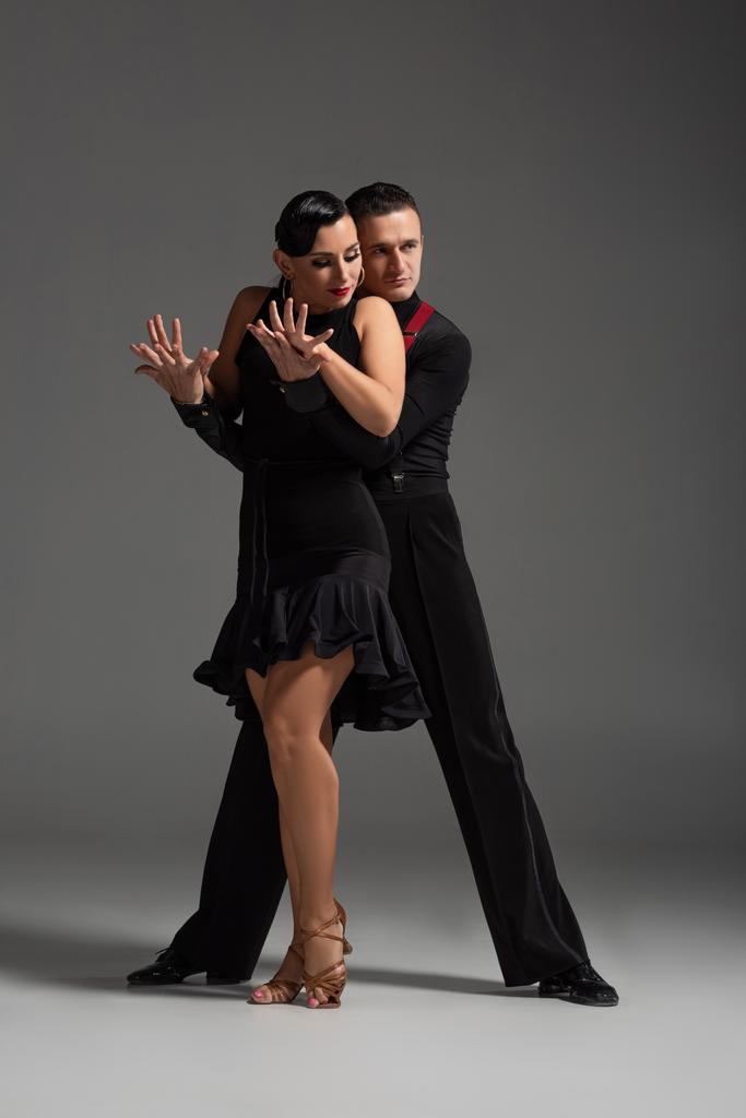 tyylikäs pari tanssijoita mustissa vaatteissa suorittamassa tangoa harmaalla taustalla
 - Valokuva, kuva