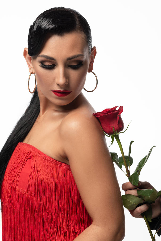 όμορφη, κομψή χορεύτρια κοιτάζοντας κόκκινο τριαντάφυλλο στο χέρι του συντρόφου, ενώ εκτελεί ταγκό απομονώνονται σε λευκό - Φωτογραφία, εικόνα