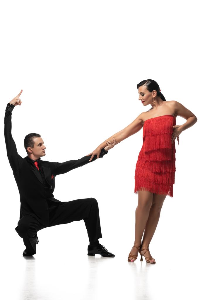 Elegante Tänzerin hockt und hält Hand ihres attraktiven Partners, während sie Tango auf weißem Hintergrund performt - Foto, Bild