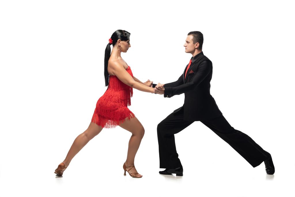 Beyaz arka planda tango yaparken el ele tutuşan ve birbirlerine bakan zarif dansçıların yan görüntüsü - Fotoğraf, Görsel