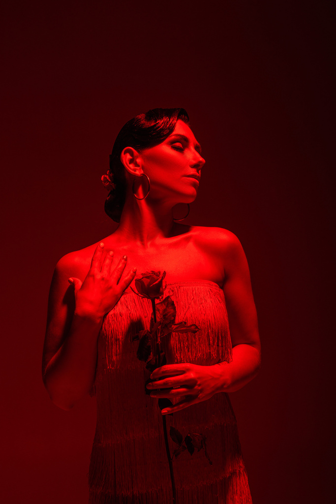 elegante tango danser met gesloten ogen met rode roos op donkere achtergrond met rode verlichting - Foto, afbeelding