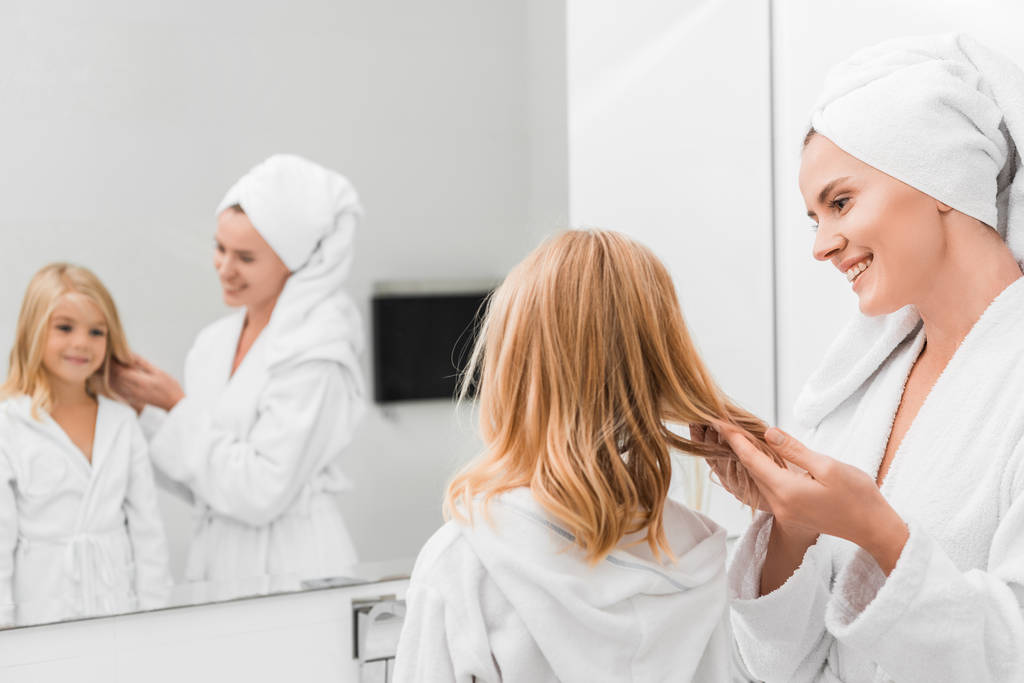 selektivní zaměření šťastné matky dotýkání vlasů roztomilé dcery v koupelně  - Fotografie, Obrázek