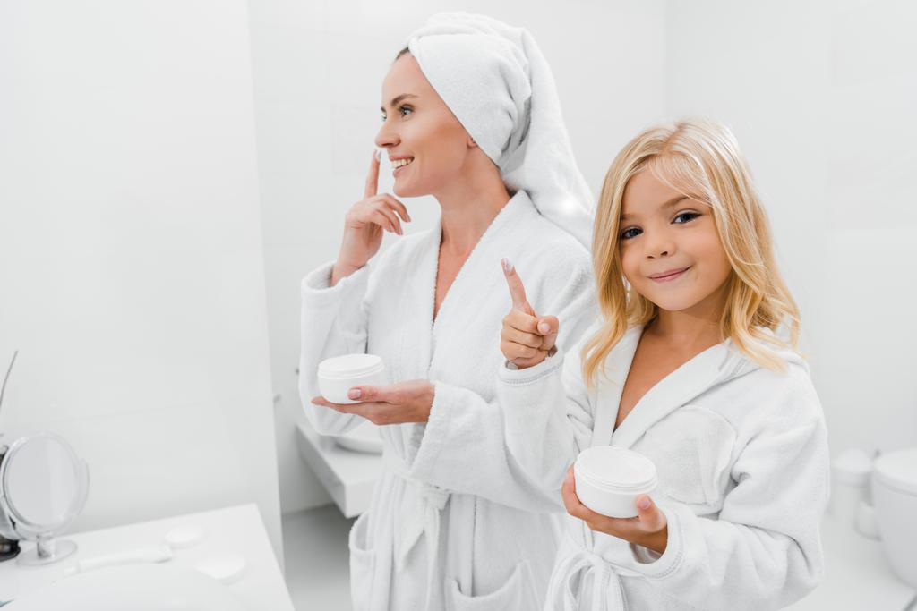 niño alegre con crema facial en el dedo cerca de la madre atractiva en el baño
  - Foto, imagen